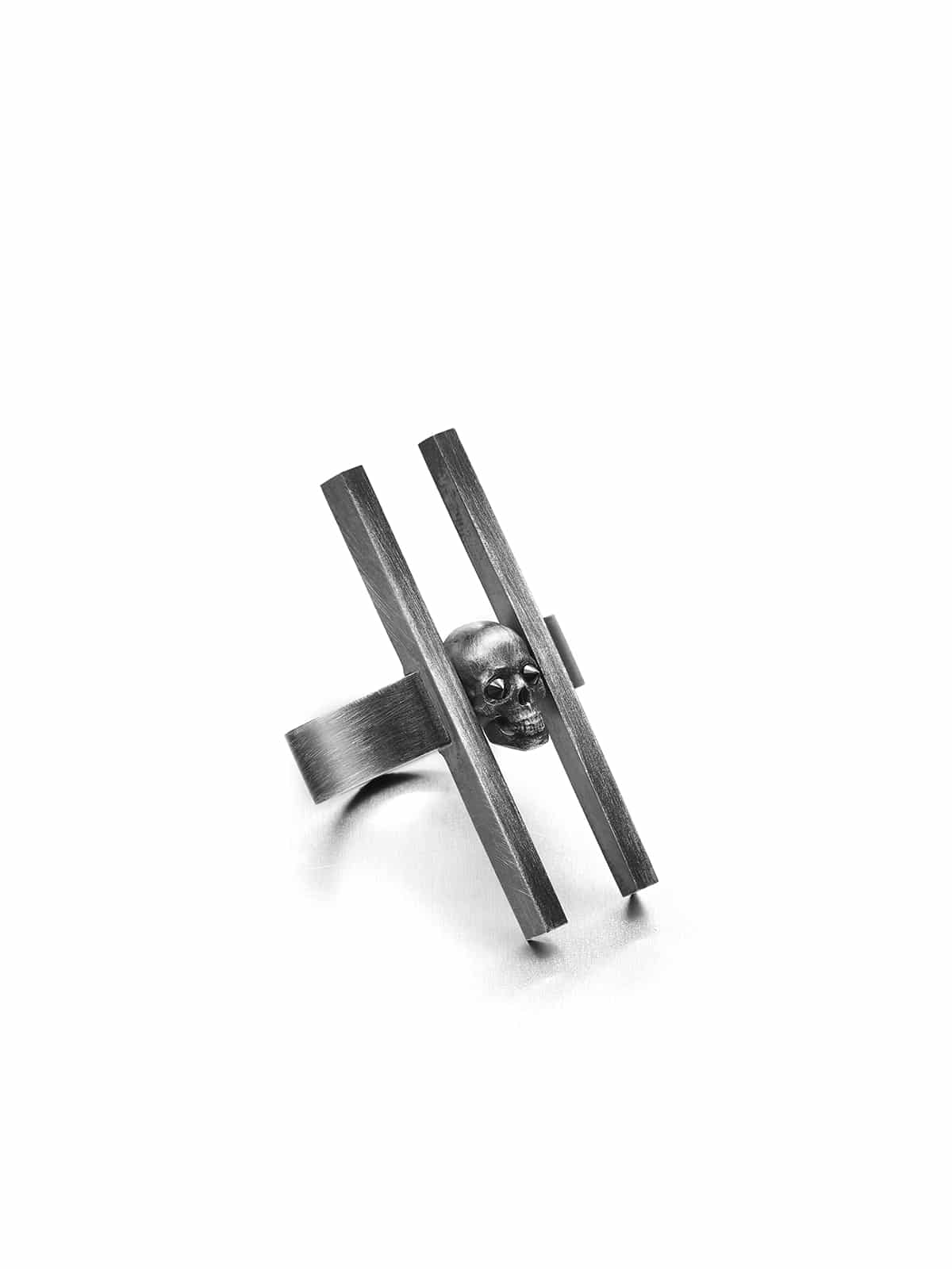 A silver ring with a central skull design, flanked by two vertical rods, with a black diamond set in the center of the skull.